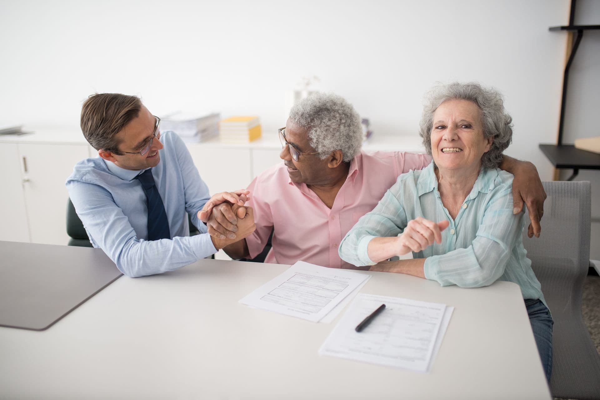 An adviser sitting with clients and shaking hands across a desk